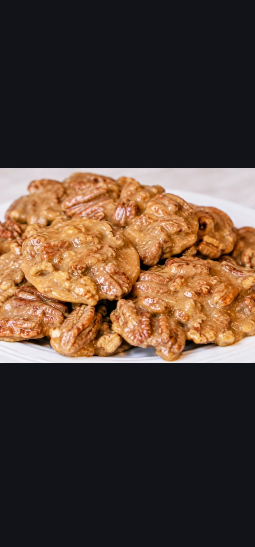 Pile of pecan pralines with a glossy caramel sugar coating on a white plate