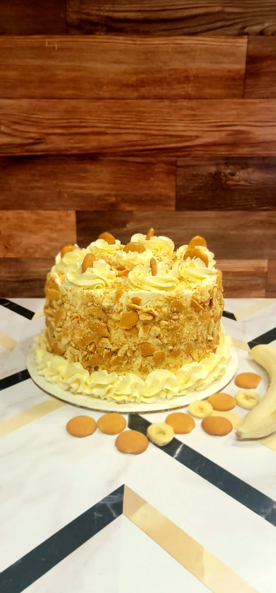 Banana pudding cake with pale yellow frosting coated in crushed vanilla wafers and topped with cream swirls