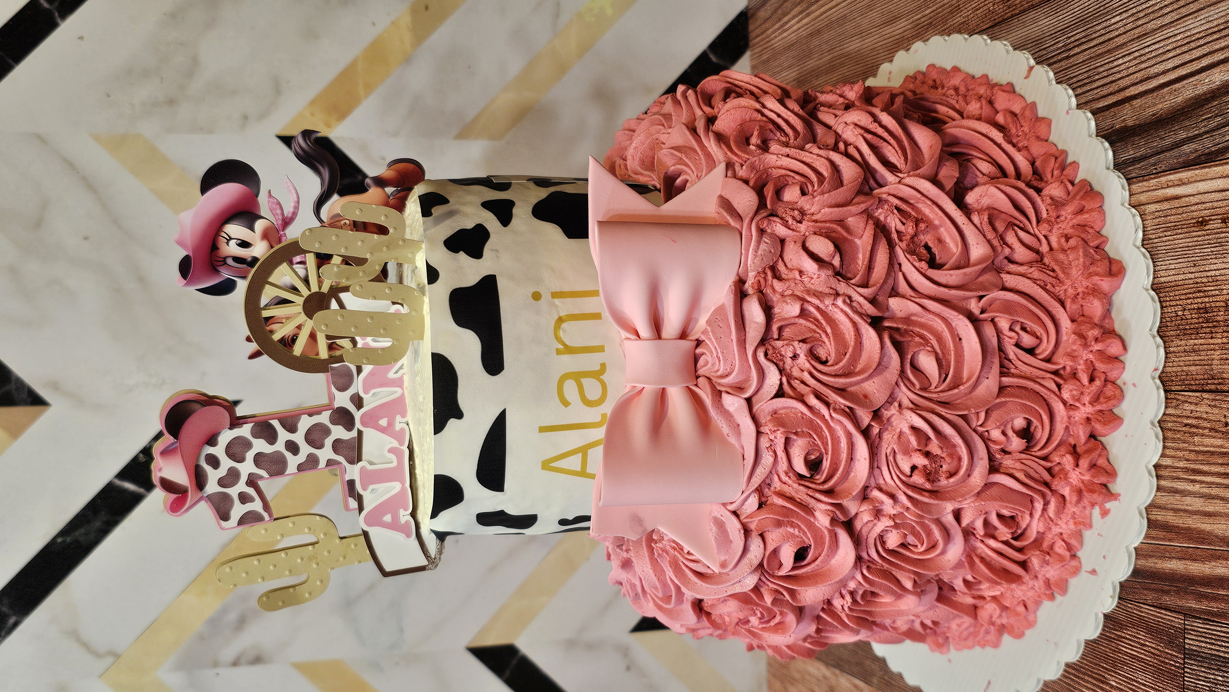 Two-tier cowgirl birthday cake with pink rosette piping and cow-print top tier