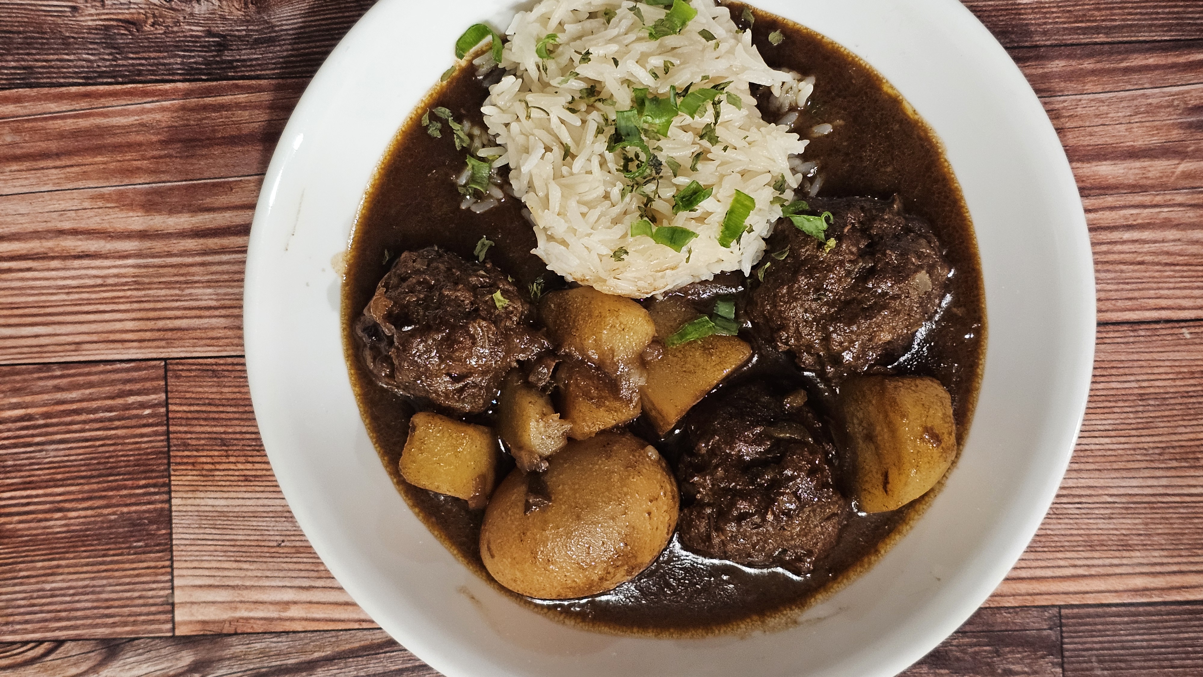 Smothered meatballs with potatoes and rice in a white bowl